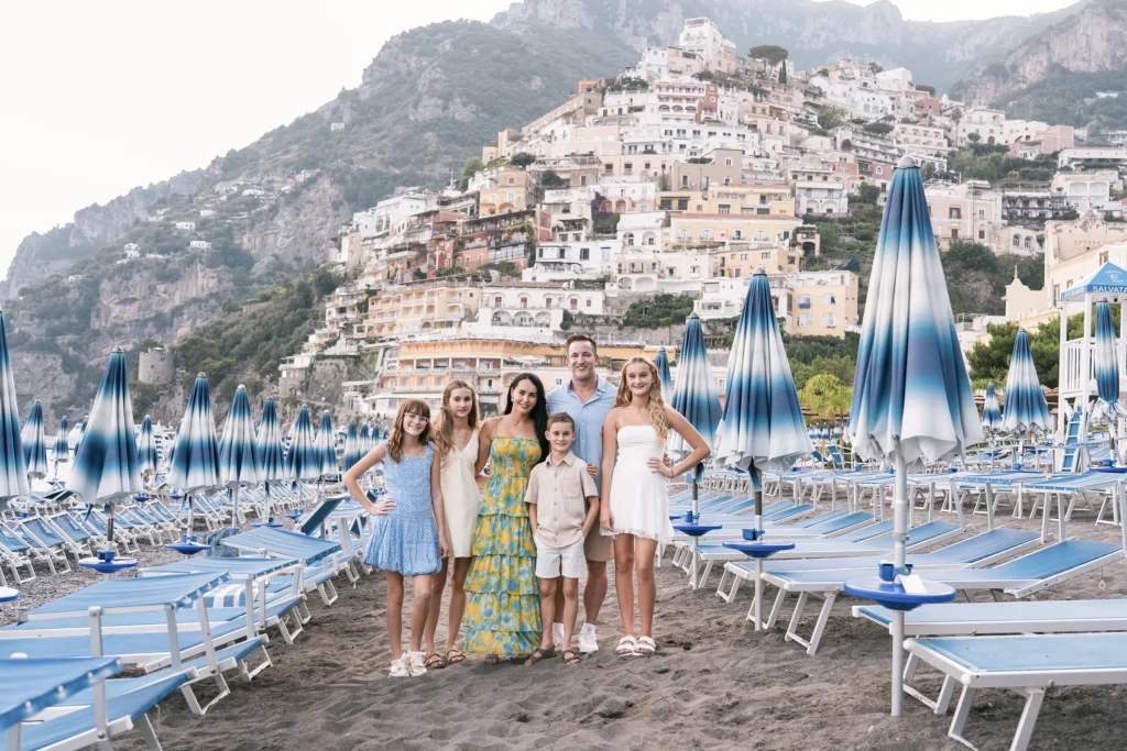 Family posing on the beach in Positano with cliffside town behind Family photoshoot in Positano on the Amalfi Coast with colorful houses in the background