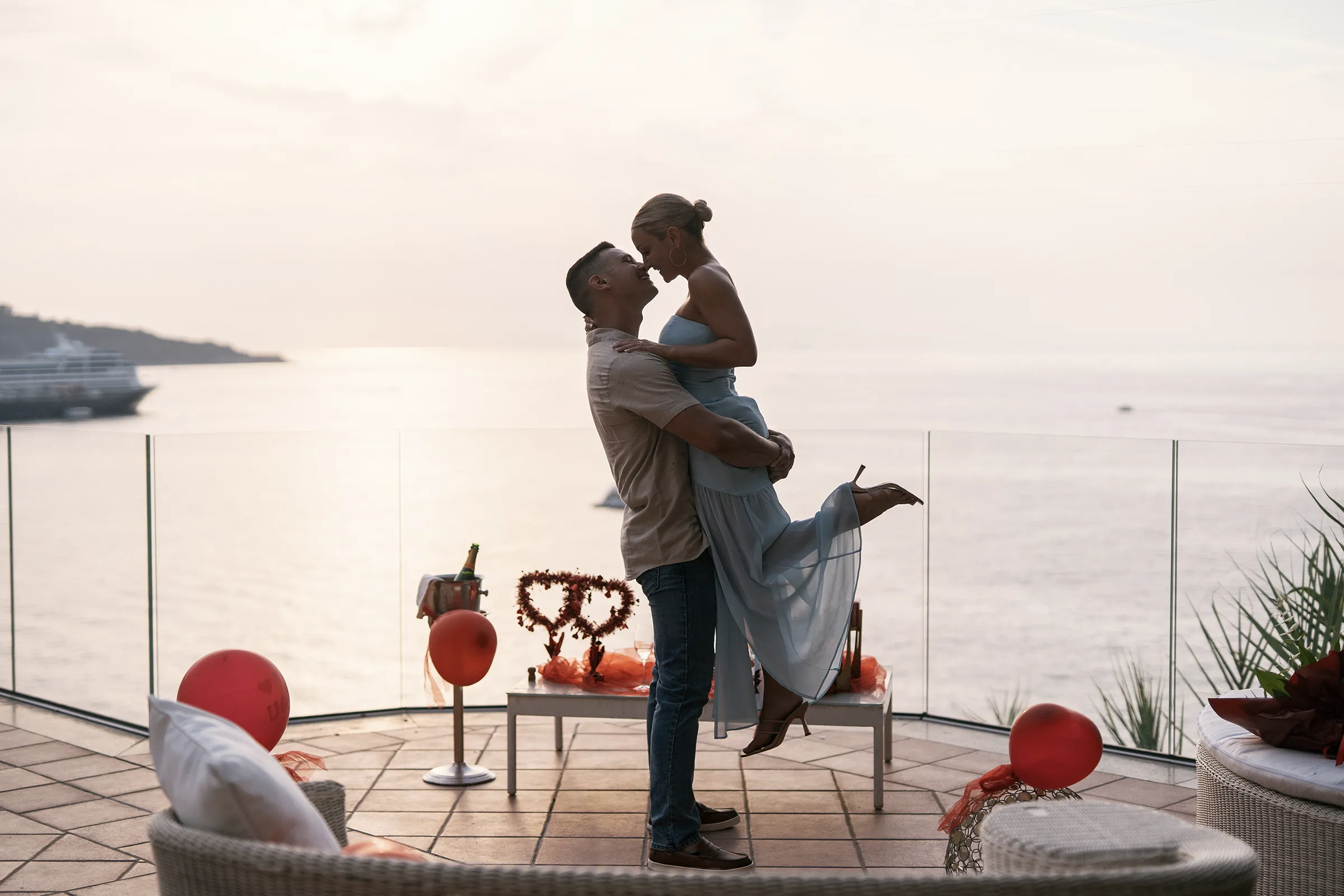 Couple embracing at sunset on a terrace decorated with red balloons and champagne
