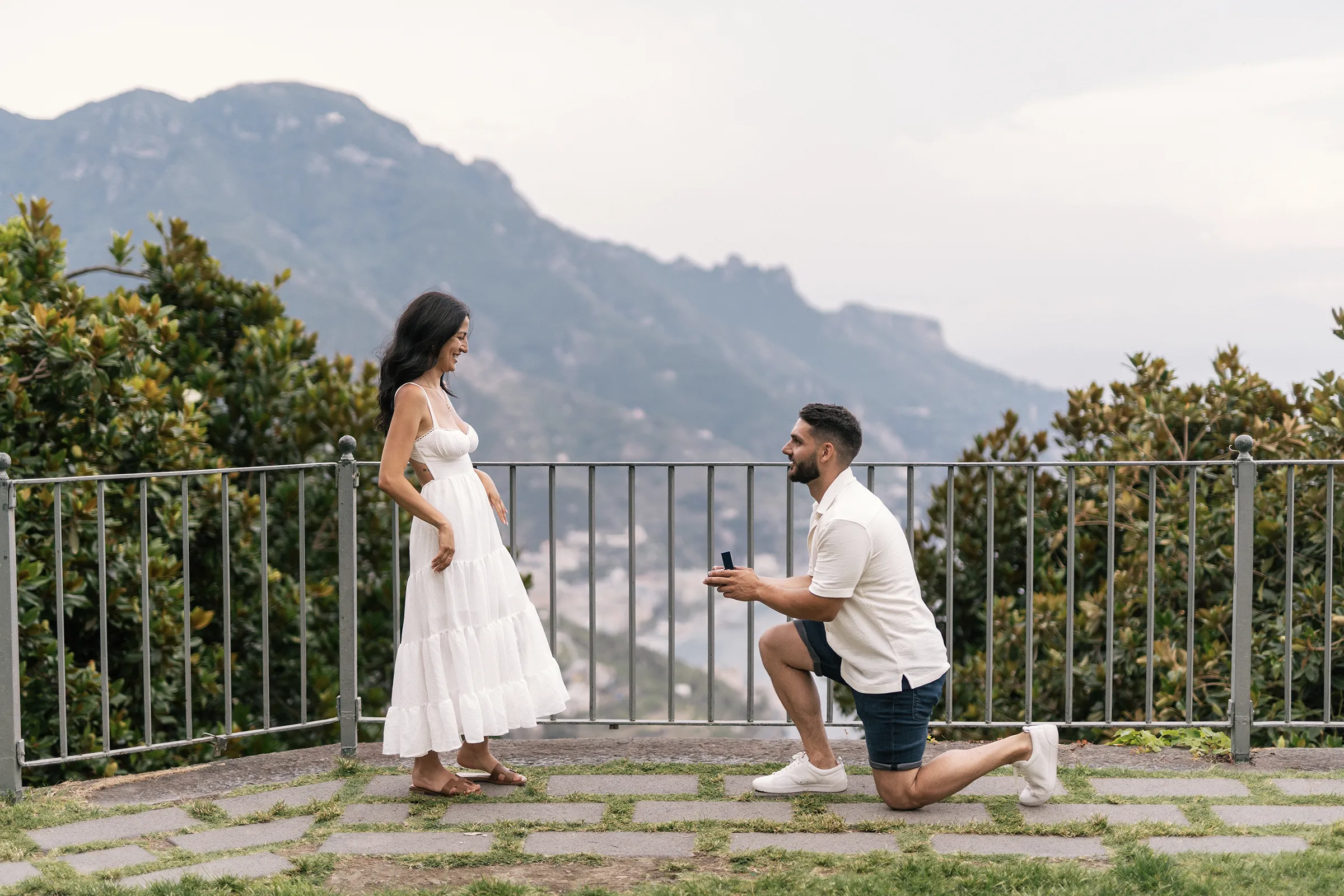 Man kneeling to propose to woman with scenic mountain and coastline background
