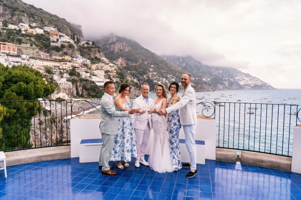 Positano destination wedding Group of six people toasting with drinks on a blue tiled terrace overlooking Positano and the Amalfi Coast.