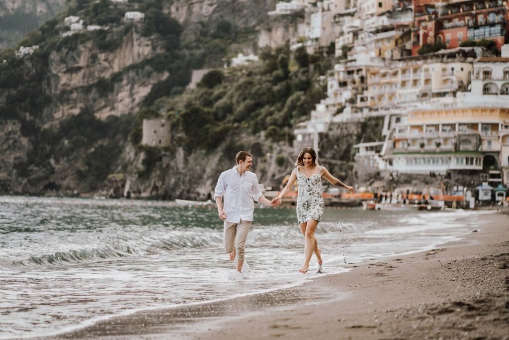 Couple walking along the beach in Positano Couple holding hands while walking along the beach in Positano with coastal buildings in the background.