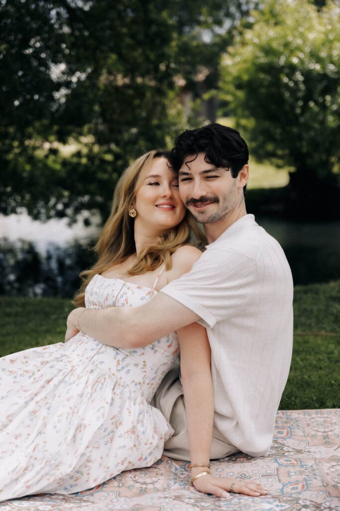 Couple embracing outdoors on a blanket in the park A smiling man and woman hugging each other while sitting on a patterned blanket in a grassy park.