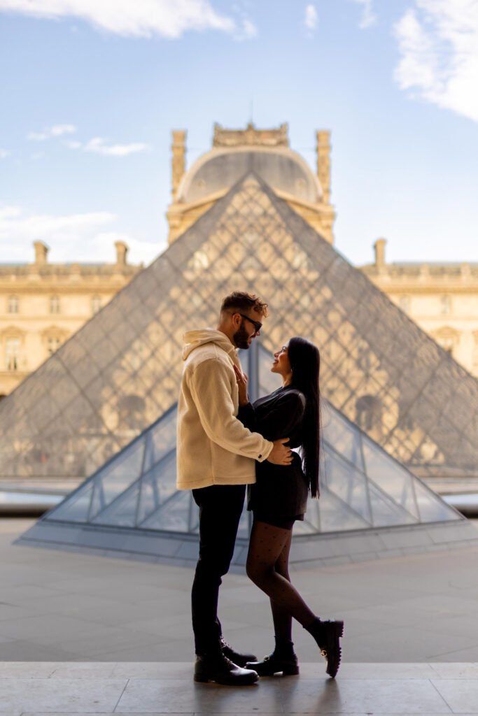 Couple embracing in front of the Louvre Pyramid in Paris A couple hugging and smiling at each other in front of the Louvre Pyramid in Paris.