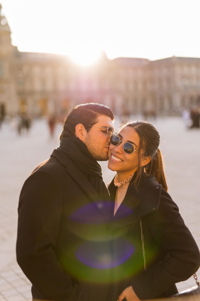 Man kissing woman on cheek during sunset Man wearing sunglasses kissing smiling woman on the cheek outdoors during sunset