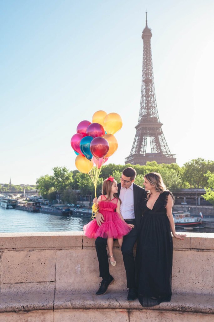 Family with colorful balloons near the Eiffel Tower in Paris Family holding colorful balloons sitting on a wall with the Eiffel Tower in Paris in the background