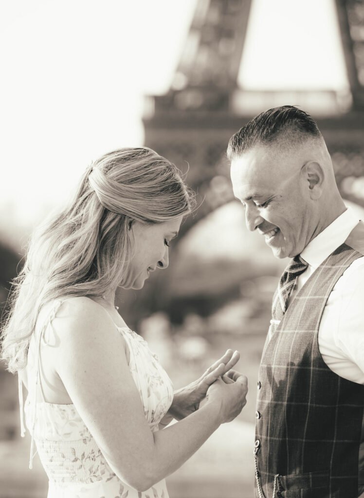 Couple exchanging rings near the Eiffel Tower in Paris Black and white photo of a couple exchanging rings with the Eiffel Tower in Paris in the background