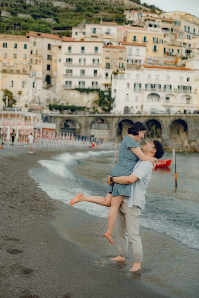 Couple hugging on the beach in Atrani along the Amalfi Coast A man lifts a woman in his arms on the sandy beach of Atrani with coastal buildings in the background.