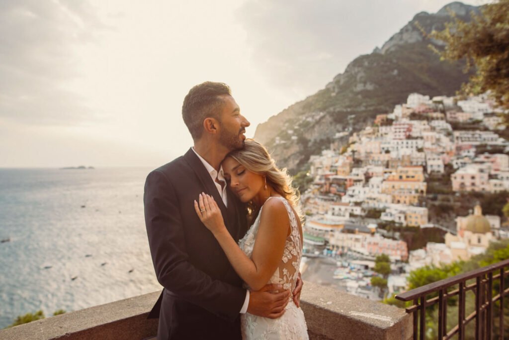 Bride and groom embracing in Positano with coastal view Bride in white dress and groom in suit embracing with Positano and the sea in the background