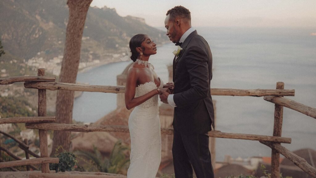 Bride and groom sharing a tender moment overlooking the Amalfi Coast Bride in a white gown and groom in a black suit standing by a wooden fence overlooking the Amalfi Coast
