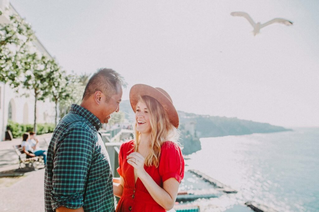 Man and woman smiling together near the coast Man in a plaid shirt and smiling woman in a red dress outdoors near the sea with a flying seagull