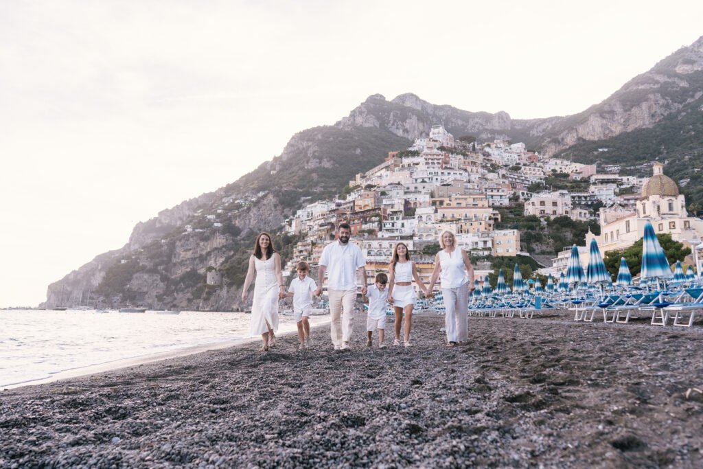 pmphoto-87 Family walking along the dark sand beach in Positano with coastal town and mountains in background